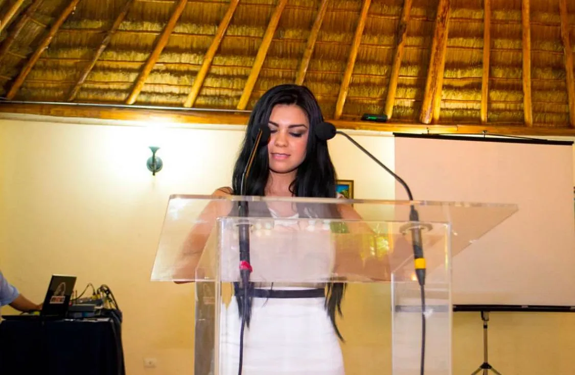 Melba habla en un podio de acrílico con micrófono